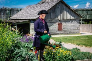 A historic interpreter watering flowers at Colonial Michilimackinac. 