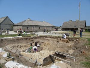 An overview photo of the archaeological excavation, showing surrounding historic buildings at Colonial Michilimackinac. 