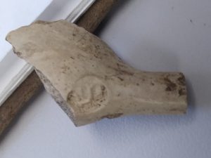 A picture of a fragment of a clay pipe with a Dutch company makers mark on it. 