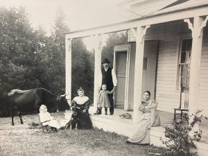 A family posing with their children, dog, cow, and kitten at the Sergeants' Quarters, behind Fort Mackinac on Mackinac Island. 