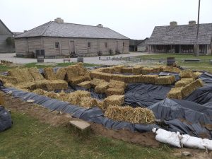 The archaeological pit filled in with a tarp and hay bales.