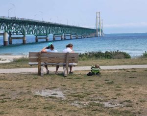 People sitting on a bench looking out at the Straits of Mackinac and the Mackinac Bridge. 