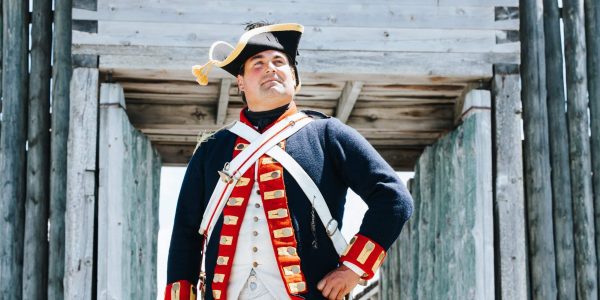 A person standing in a blue coat with a tri-corn hat, looking in the distance.